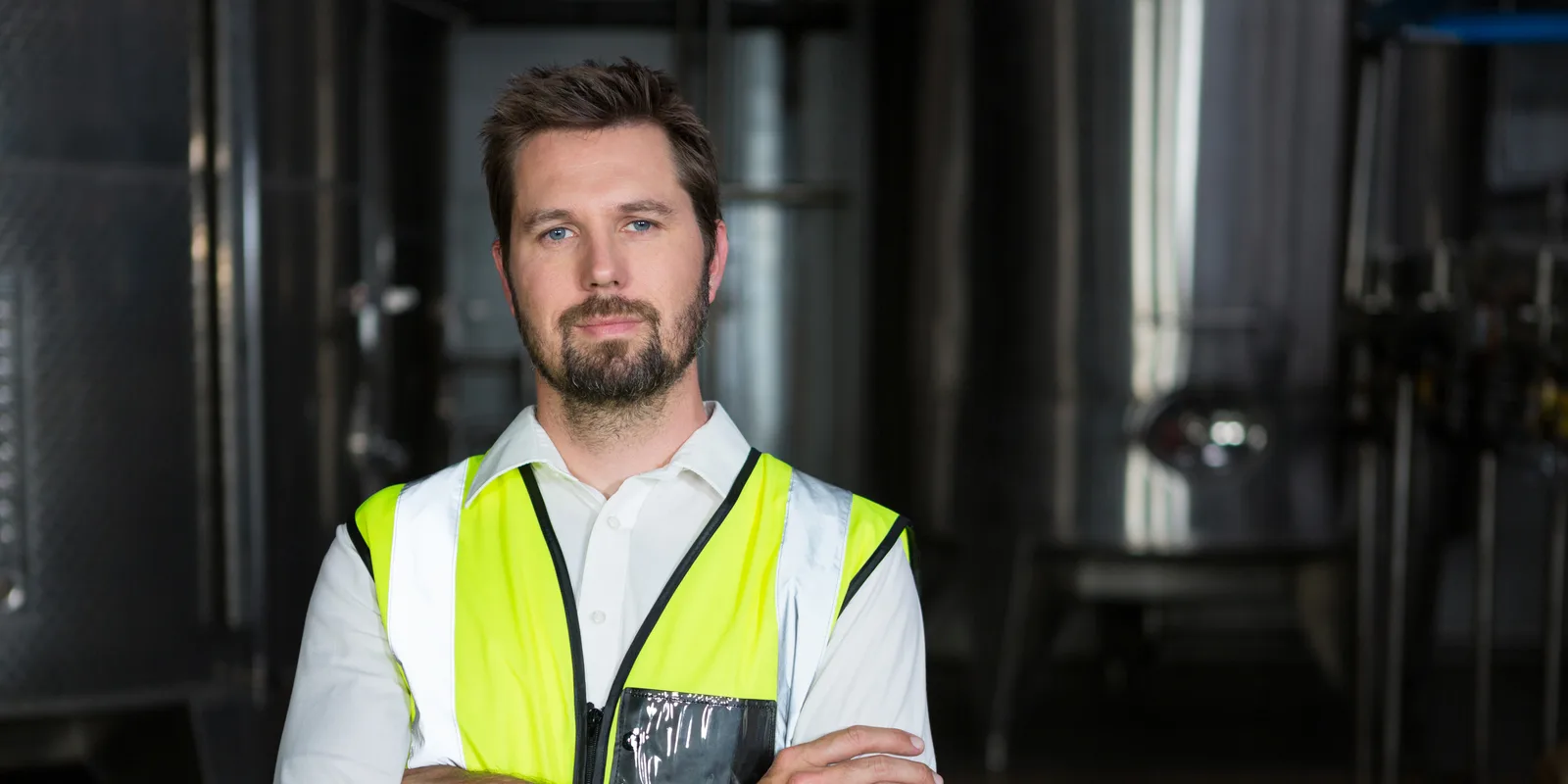 Un technicien en gilet haute visibilité, bras croisés, dans un atelier industriel